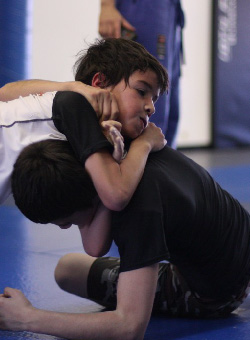 Close-up of two male children practicing jiu-jitsu. One kid has a triangle arm choke one the other kid.